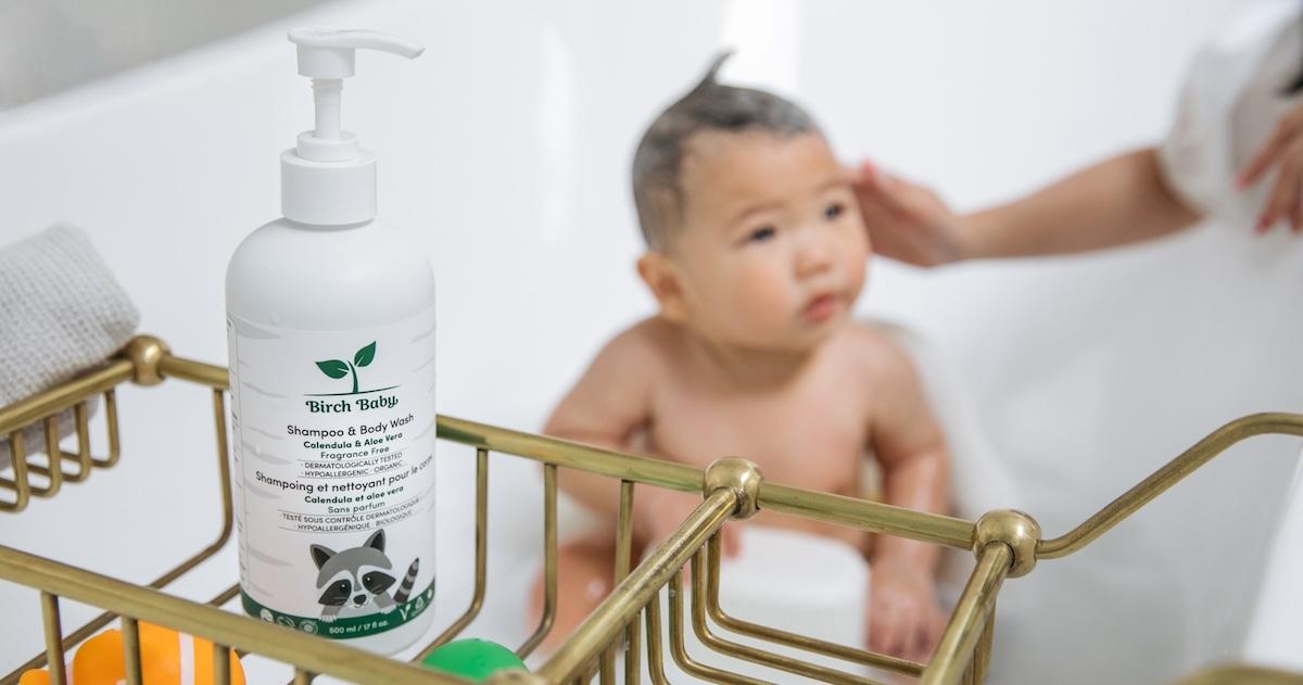 Baby in bath in the background, with a bottle of Birch Baby Shampoo & Body Wash in the foreground.