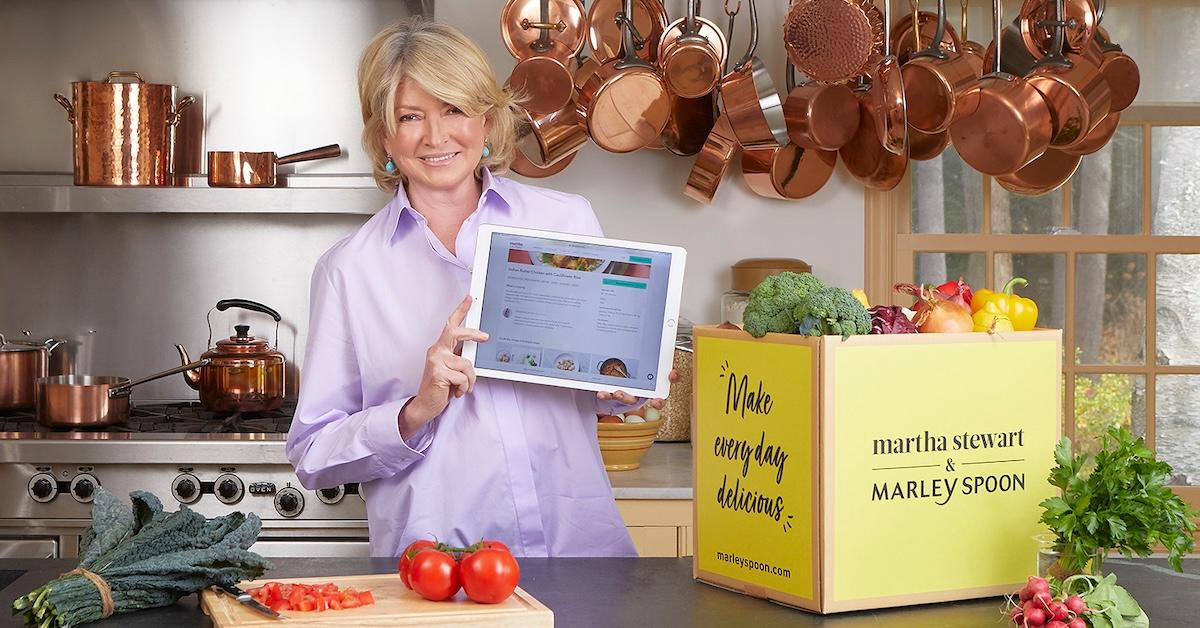 Martha Stewart holds an iPad at a kitchen island, along with a Marley Spoon box and vegetables.