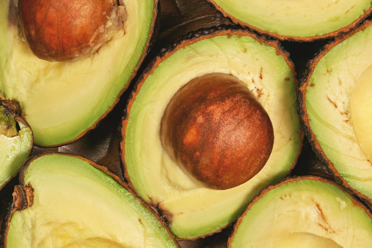 A pit is featured in the center of a photo of several avocado halves laying beside one another.