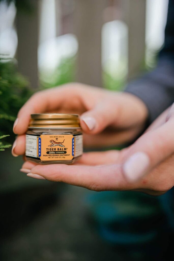 Woman displaying a jar of Tiger Balm to illustrate the benefits of Tiger Balm