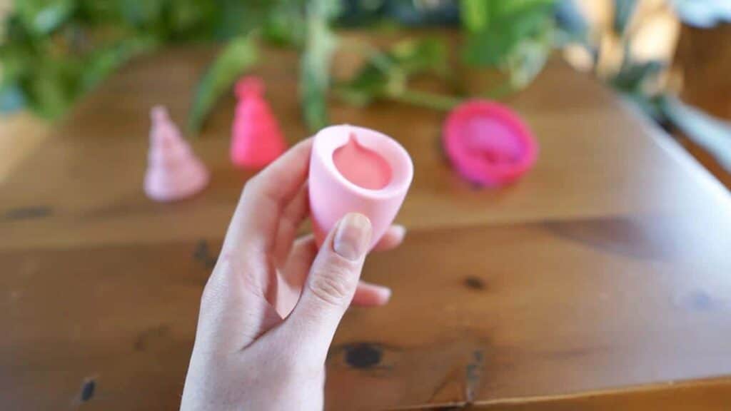 A woman's hand holding a soft, pink menstrual cups