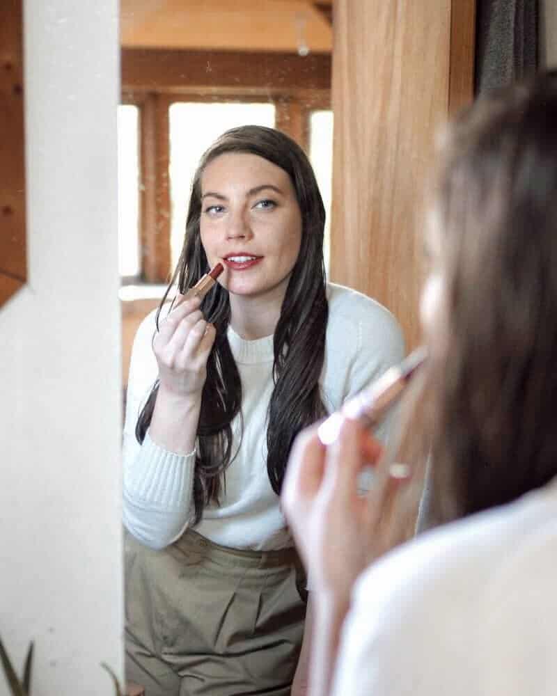 Woman applying red lipstick and finding joy in life through self care. 