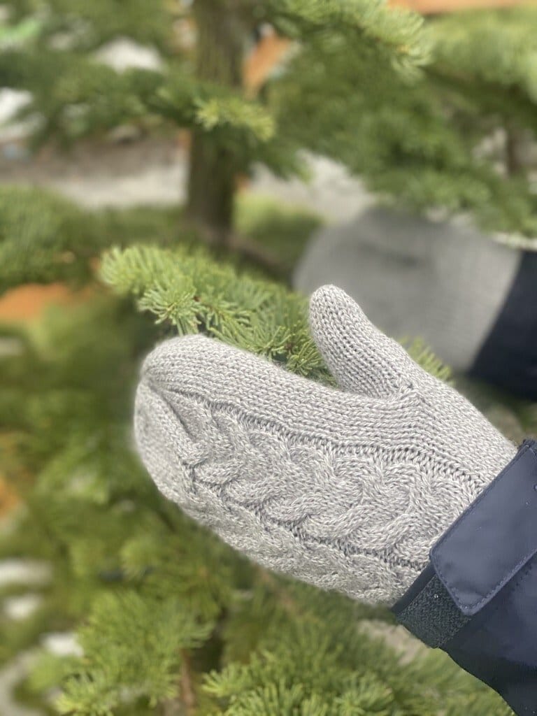 Digital detox challenge: woman wearing a knife mittens touching an evergreen tree to illustrate a post about a digital detox.